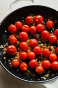 Cherry tomatoes, onion, and garlic cooking in a skillet