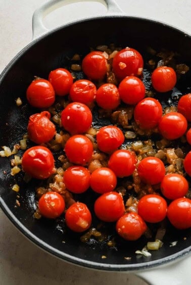 Cherry tomatoes, onion, and garlic cooking in a skillet