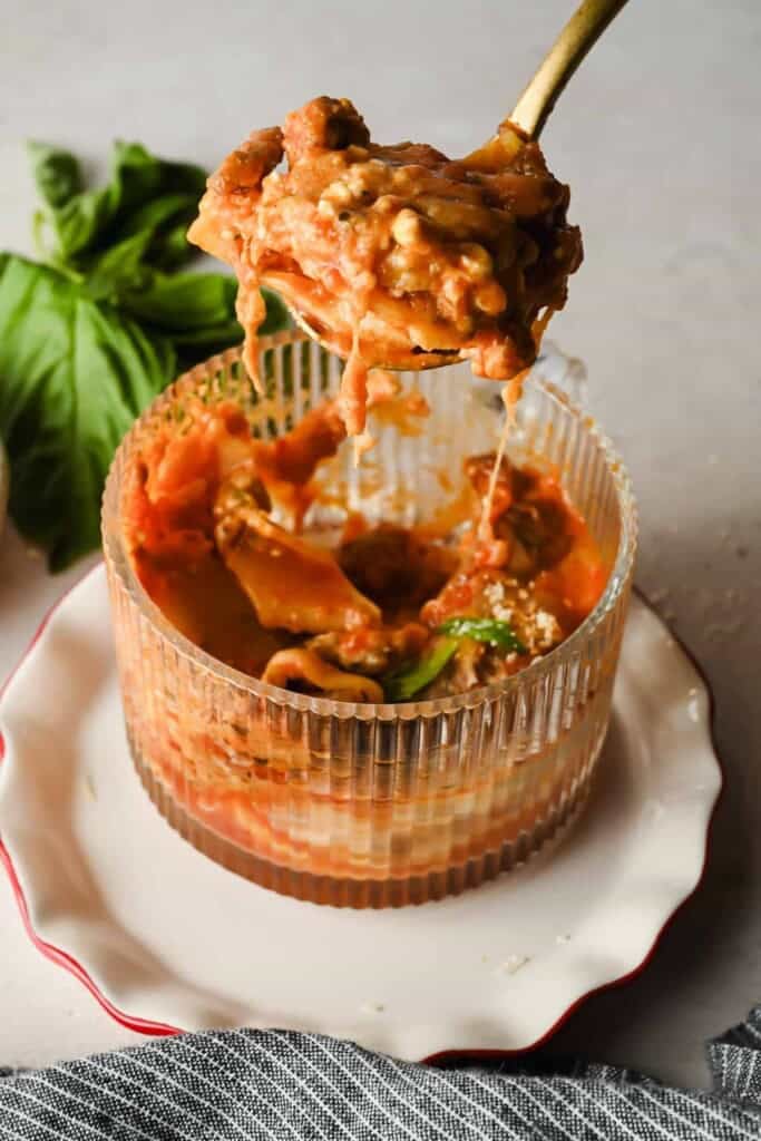 Spoon lifting layers of microwave lasagna showing melted cheese and meat sauce
