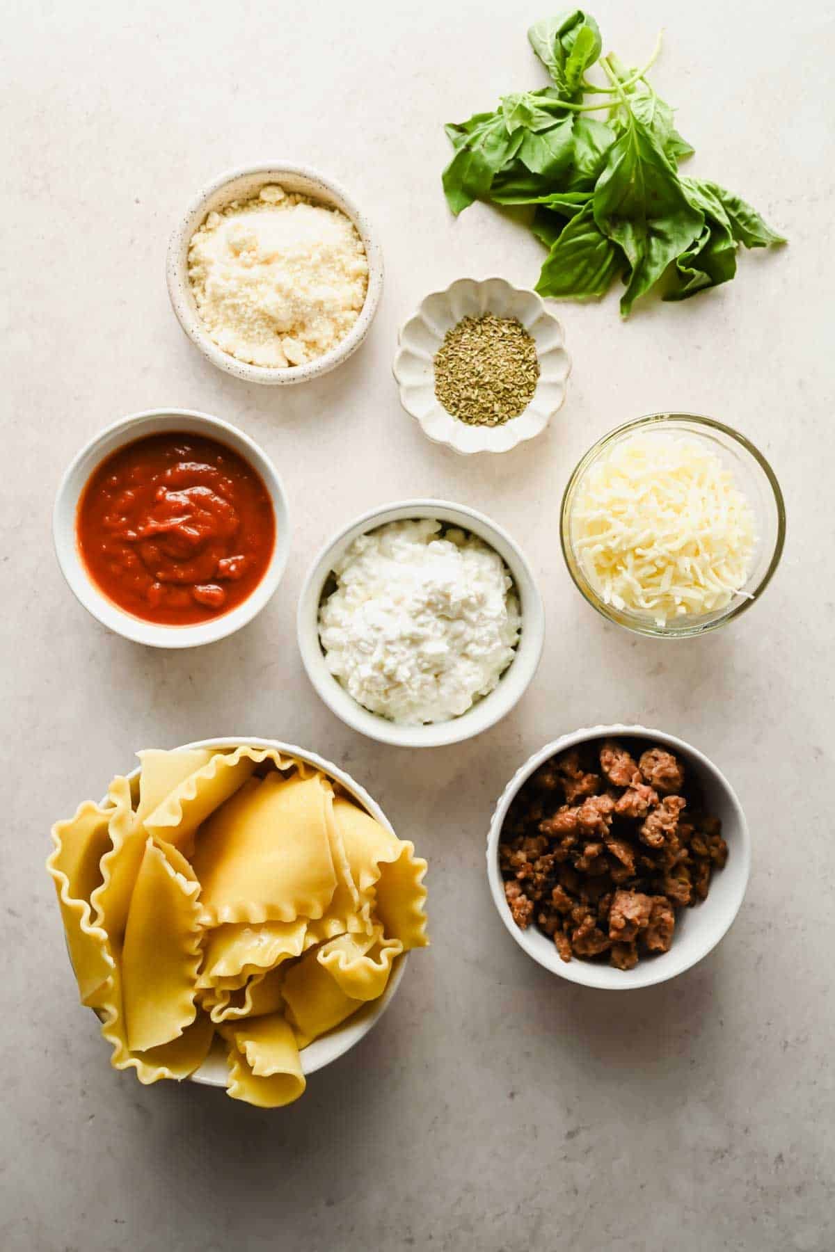 Ingredients for microwave lasagna laid out including lasagna noodles cottage cheese marinara mozzarella sausage and basil