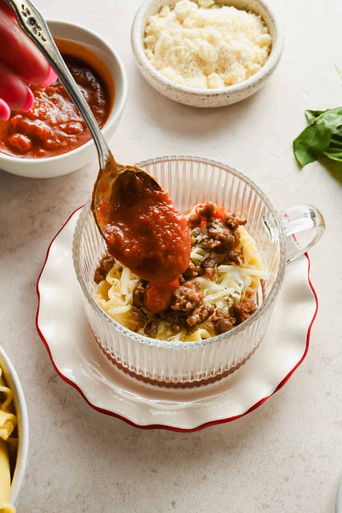 Spooning marinara sauce over lasagna layers in a mug