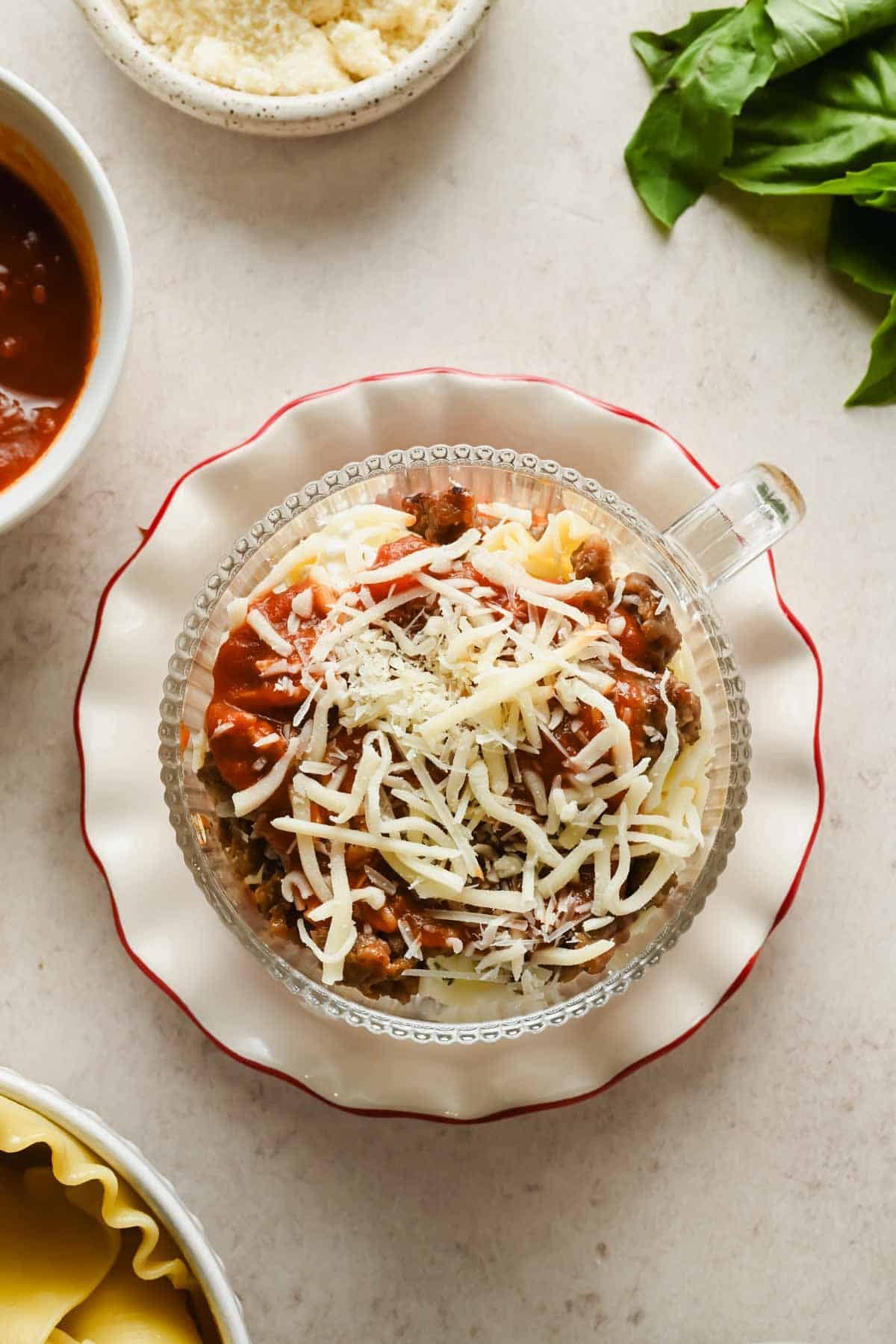 Overhead view of assembled microwave lasagna in a mug topped with shredded mozzarella