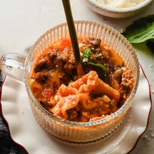 Microwave lasagna in a mug topped with melted cheese and fresh basil