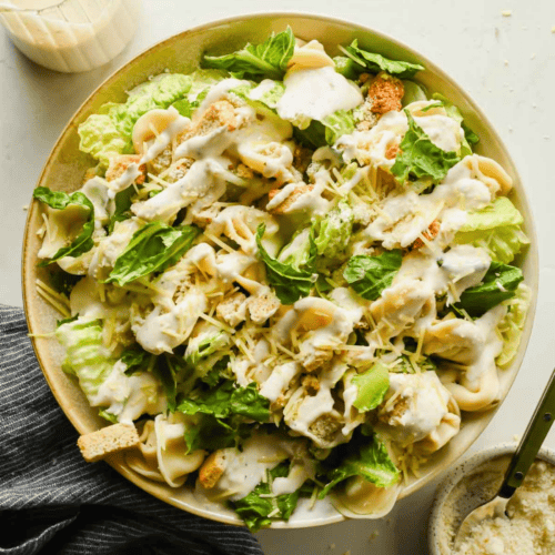 Bowl of tortellini Caesar salad with lettuce, croutons, pasta shells, grated cheese, and creamy dressing, viewed from above.