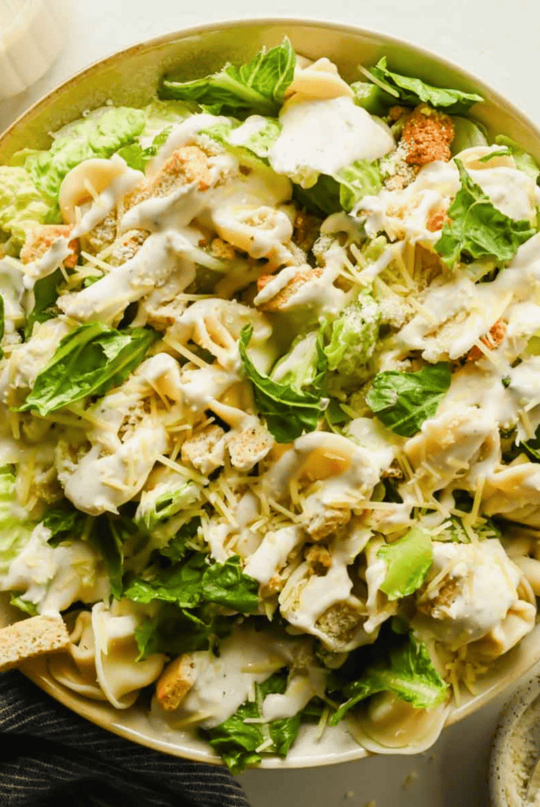 Bowl of tortellini Caesar salad with lettuce, croutons, pasta shells, grated cheese, and creamy dressing, viewed from above.