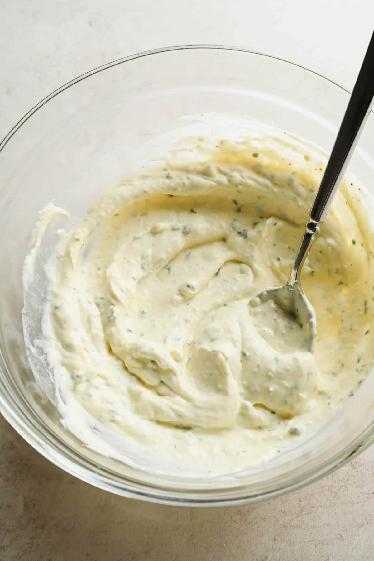 Close-up of smooth garlic and herb Boursin dressing in a glass mixing bowl.