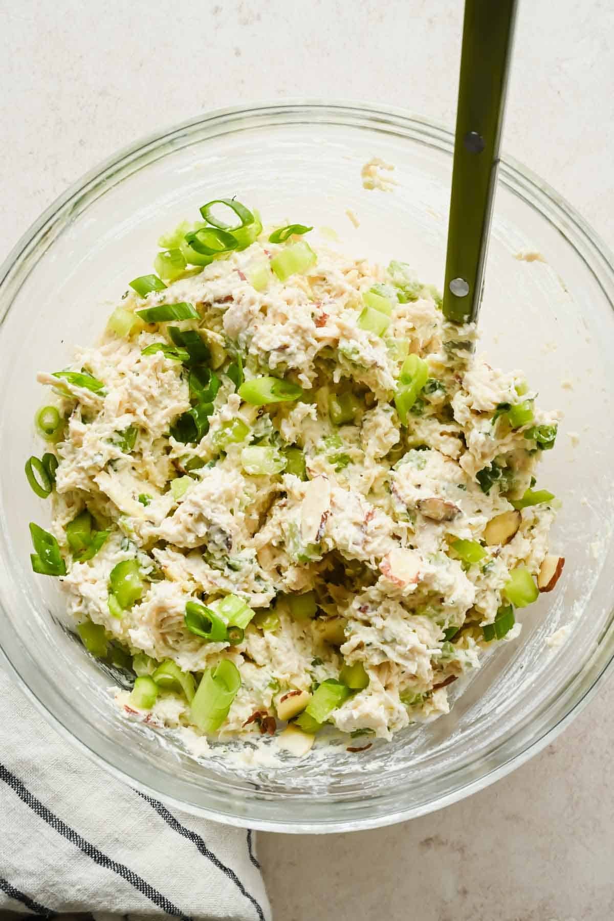 Boursin chicken salad spread fully combined with celery, green onions, and sliced almonds in a glass bowl.