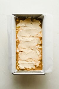 Cream cheese filling spread over apple bread batter in a loaf pan