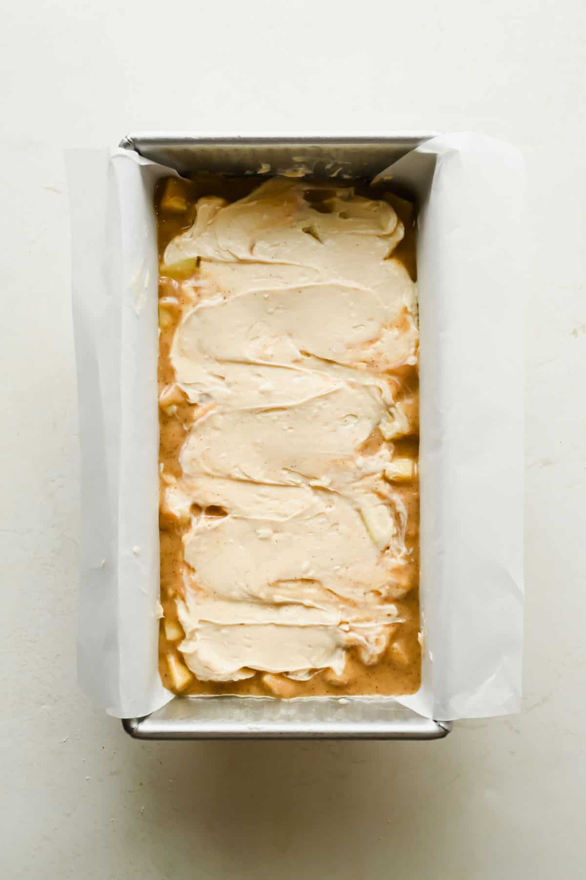 Cream cheese filling spread over apple bread batter in a loaf pan