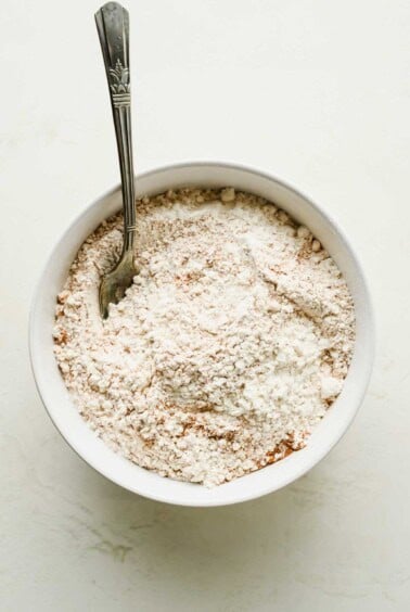 Flour, baking powder, salt, cinnamon, and nutmeg in a white bowl