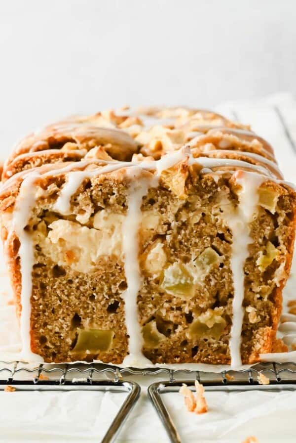 Sliced cream cheese apple fritter bread showing diced apples, glaze, and a cream cheese stripe
