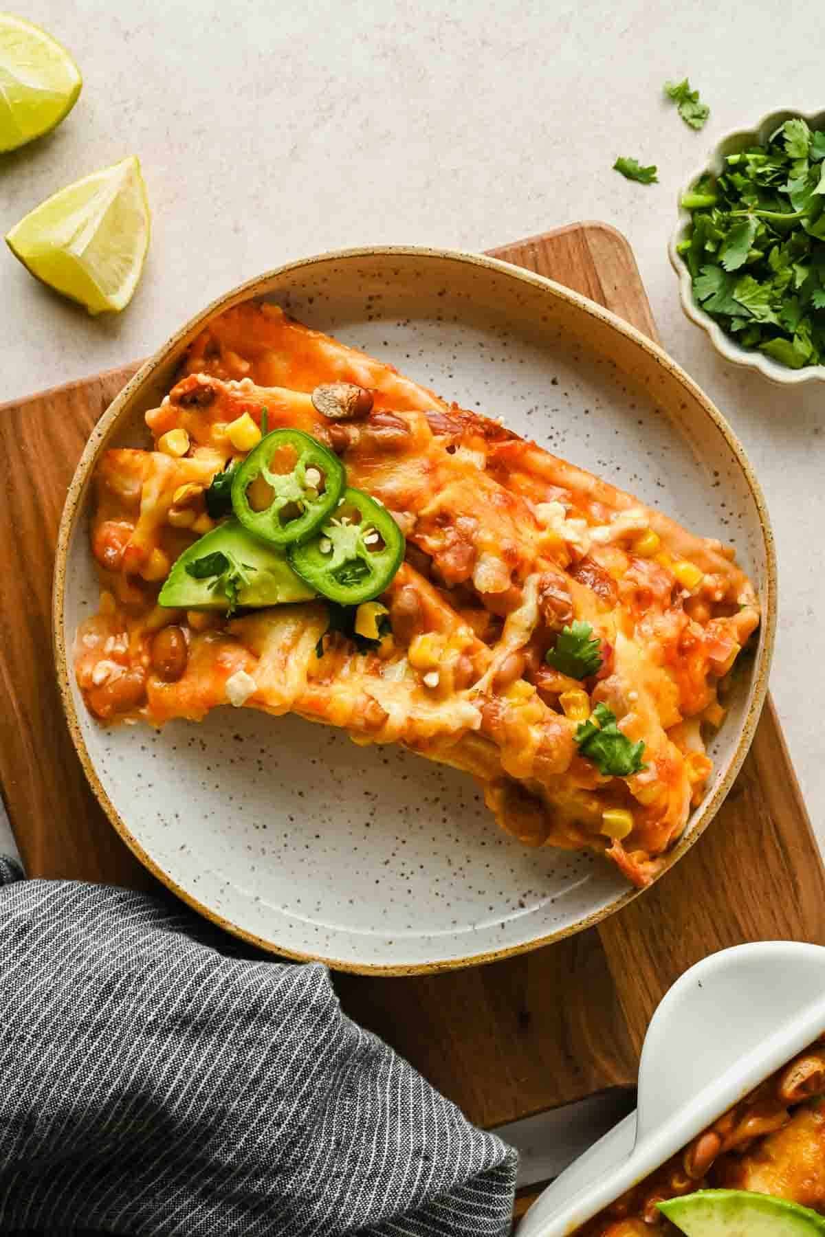 A scoop of saucy, cheesy folded tortillas with beans and corn on a plate, topped with avocado and jalapeño.