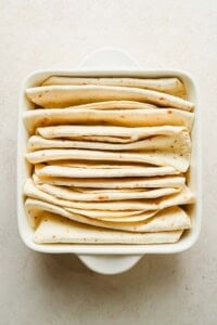 Flour tortillas folded into upright pleats and arranged in a square baking dish.