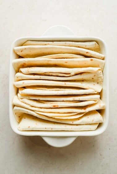 Flour tortillas folded into upright pleats and arranged in a square baking dish.