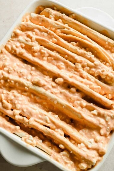 Close-up of folded flour tortillas coated with creamy enchilada sauce in a baking dish.