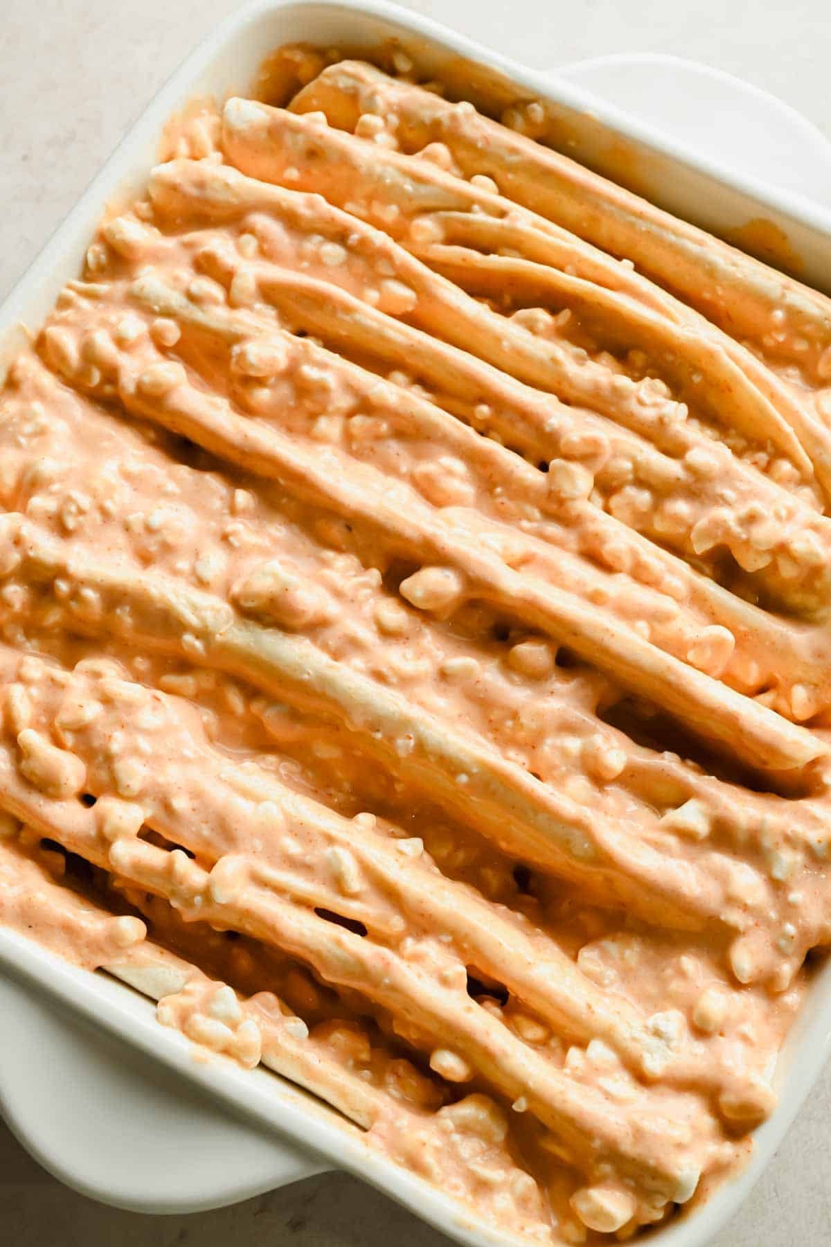 Close-up of folded flour tortillas coated with creamy enchilada sauce in a baking dish.