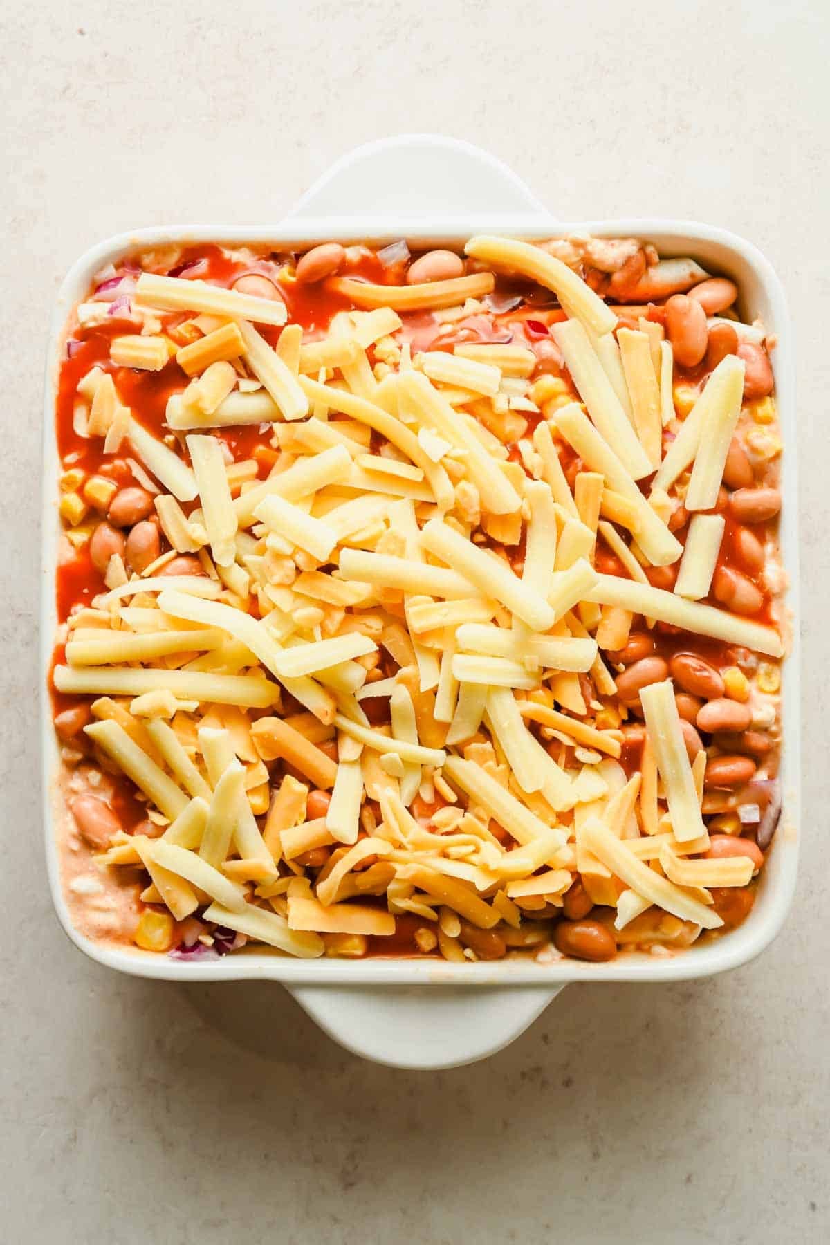 Shredded cheese and enchilada sauce cover the bean-and-corn tortilla bake before it goes into the oven.