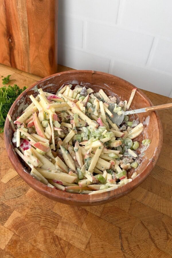 Apple celery salad with walnuts in a creamy dressing inside a wooden bowl with a serving spoon.