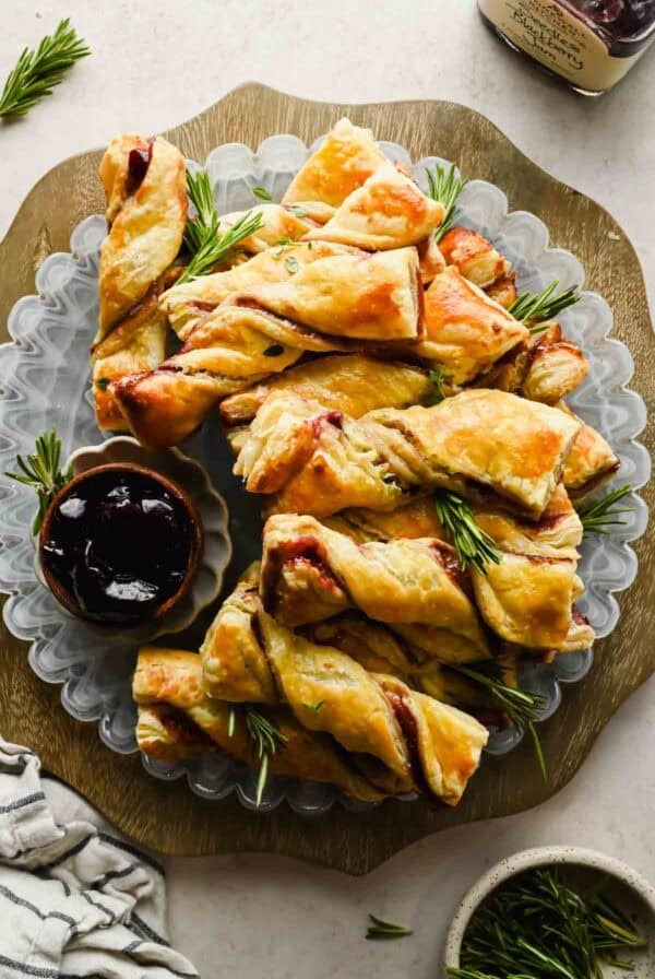 Blackberry Boursin puff pastry twists arranged on a platter with herbs and a bowl of jam.