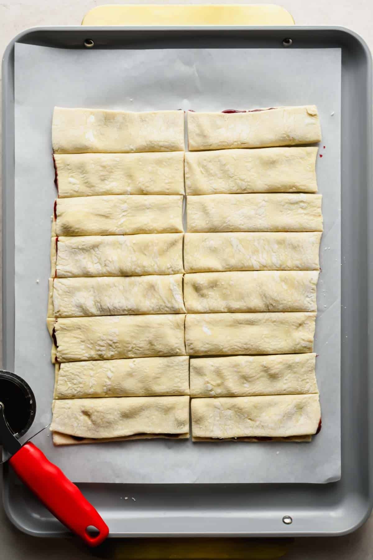 Filled puff pastry cut in half and into 16 strips on a baking sheet.