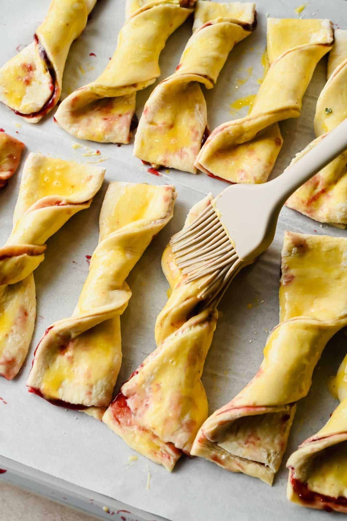 Brushing whisked egg onto unbaked blackberry Boursin puff pastry twists.