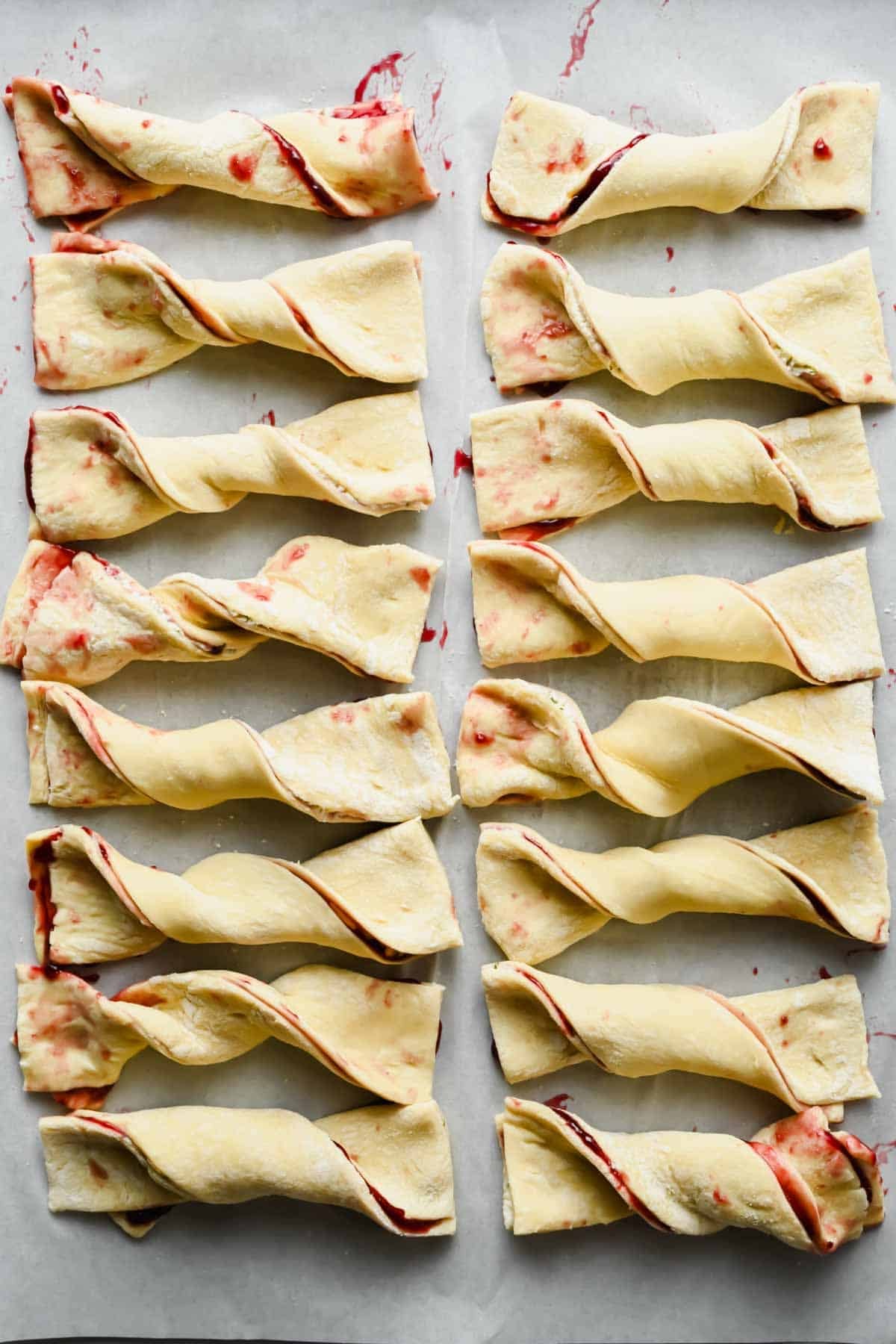 Sixteen unbaked blackberry Boursin pastry twists arranged on parchment paper.