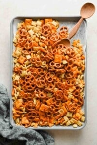 Cheesy Chex mix spread across a parchment-lined rimmed baking sheet.
