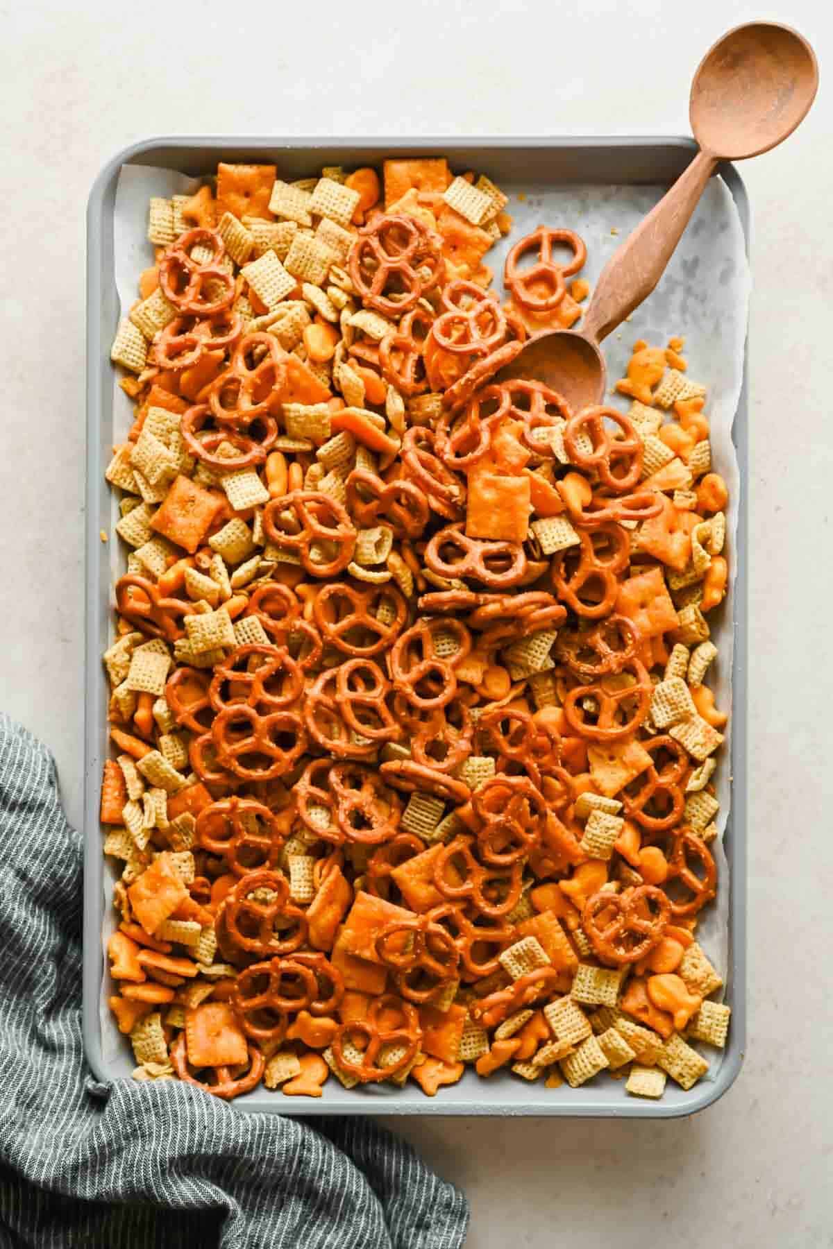 Cheesy Chex mix spread across a parchment-lined rimmed baking sheet.