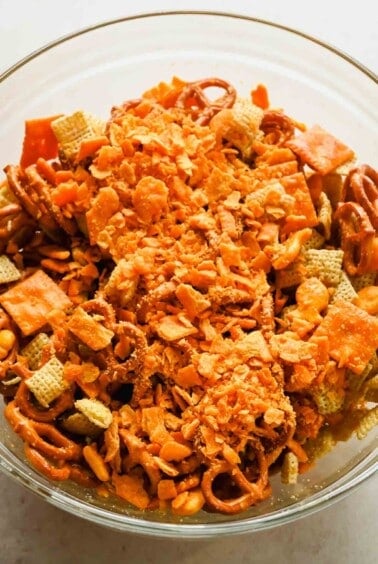 Finely crushed Cheez-Its added to the seasoned Chex mix in a glass bowl.