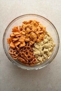 Rice Chex, Cheez-Its, Goldfish, and pretzels in a glass mixing bowl before seasoning.