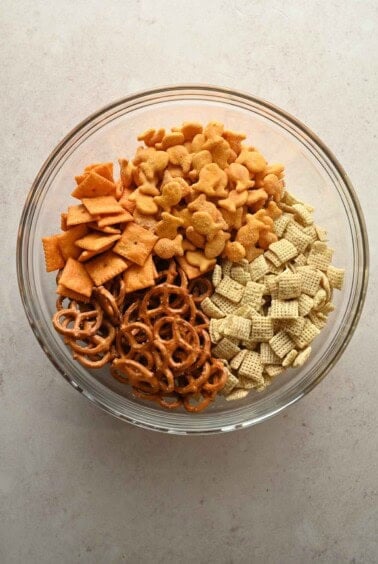 Rice Chex, Cheez-Its, Goldfish, and pretzels in a glass mixing bowl before seasoning.
