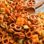 Finished cheesy Chex mix with pretzels, Rice Chex, Cheez-Its, and Goldfish in a bowl with a wooden spoon.