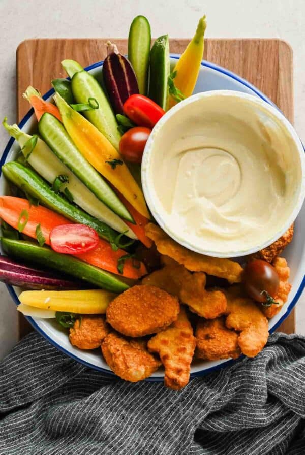 A bowl of cottage cheese honey mustard dip with chicken nuggets, carrots, cucumbers, and tomatoes.