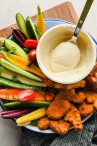 A spoonful of honey mustard dip beside chicken nuggets and vegetables.