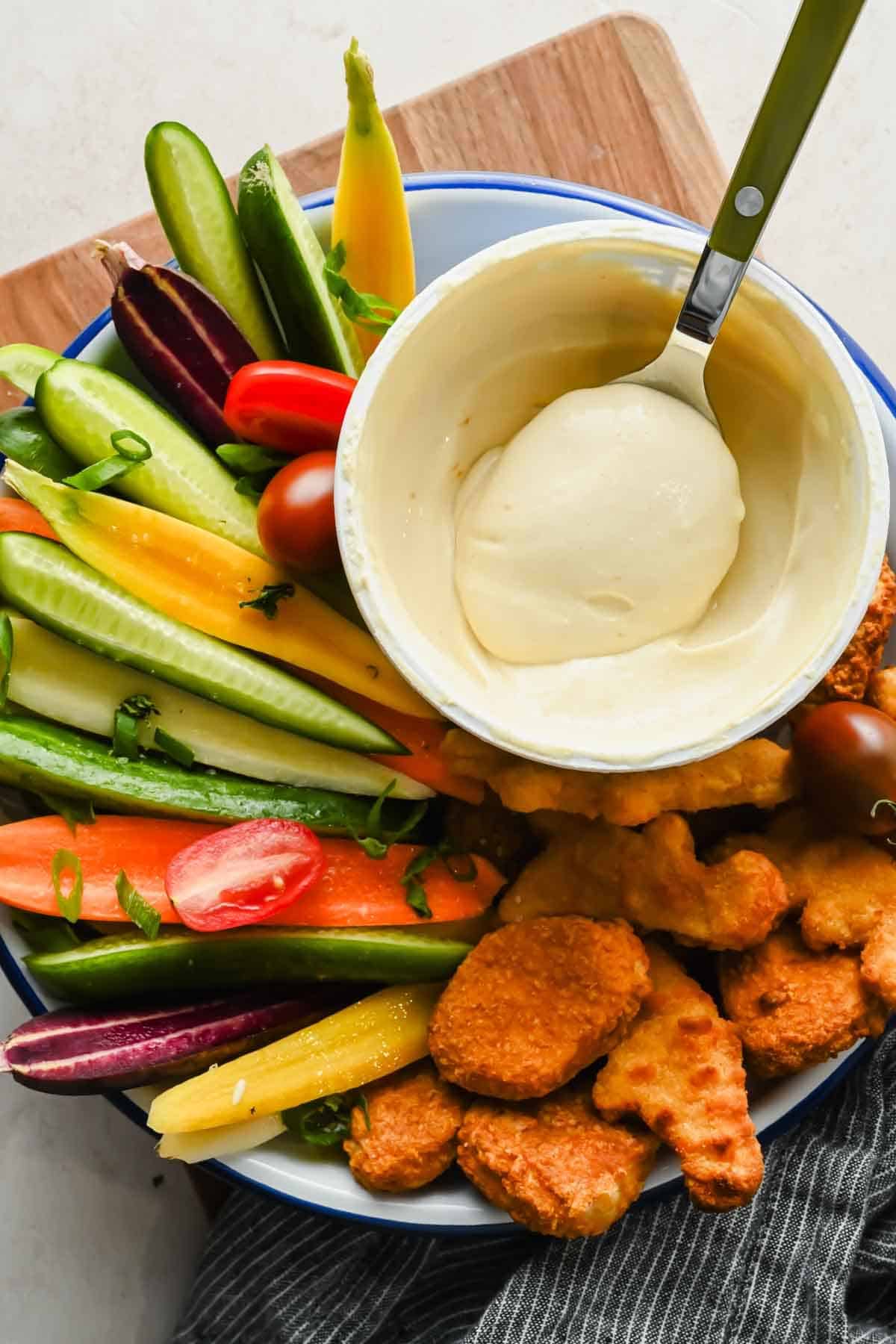 A spoonful of honey mustard dip beside chicken nuggets and vegetables.