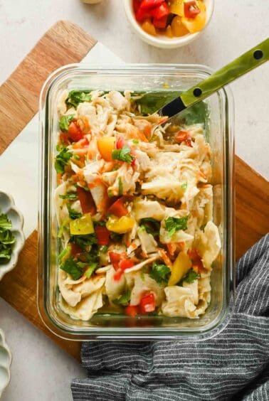 Single-serving chicken enchilada topped with diced tomatoes and cilantro in a glass container.