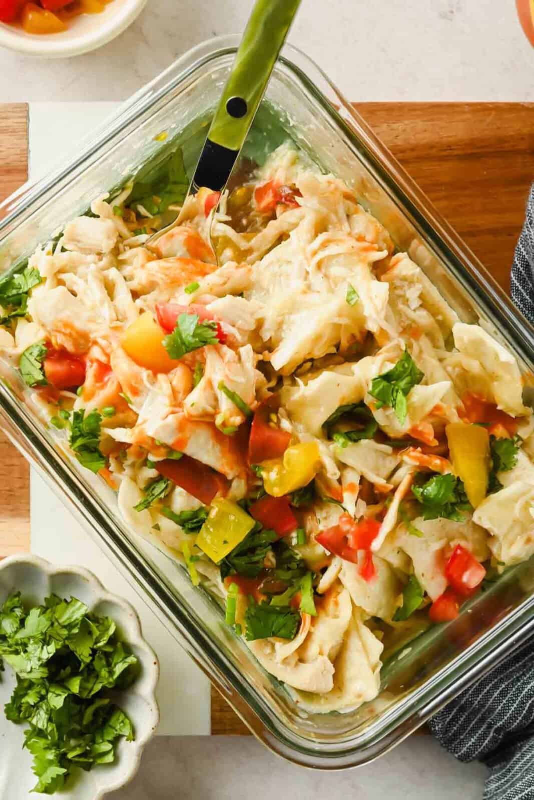 Single-serving chicken enchilada topped with diced tomatoes and cilantro in a glass container.