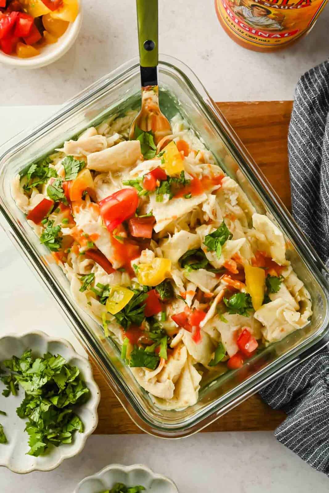 Single-serving chicken enchilada topped with diced tomatoes and cilantro in a glass container.